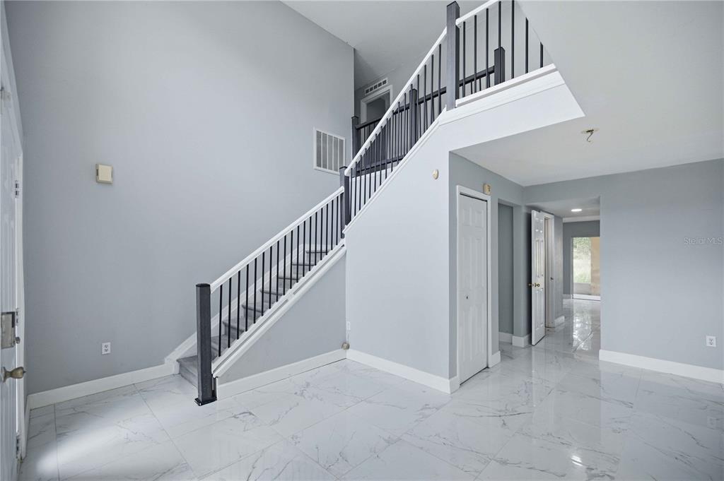 A bright entryway features white marble-look tile flooring, light gray walls, and a wooden staircase — 4517 SE 31ST PLACE, OCALA, FL