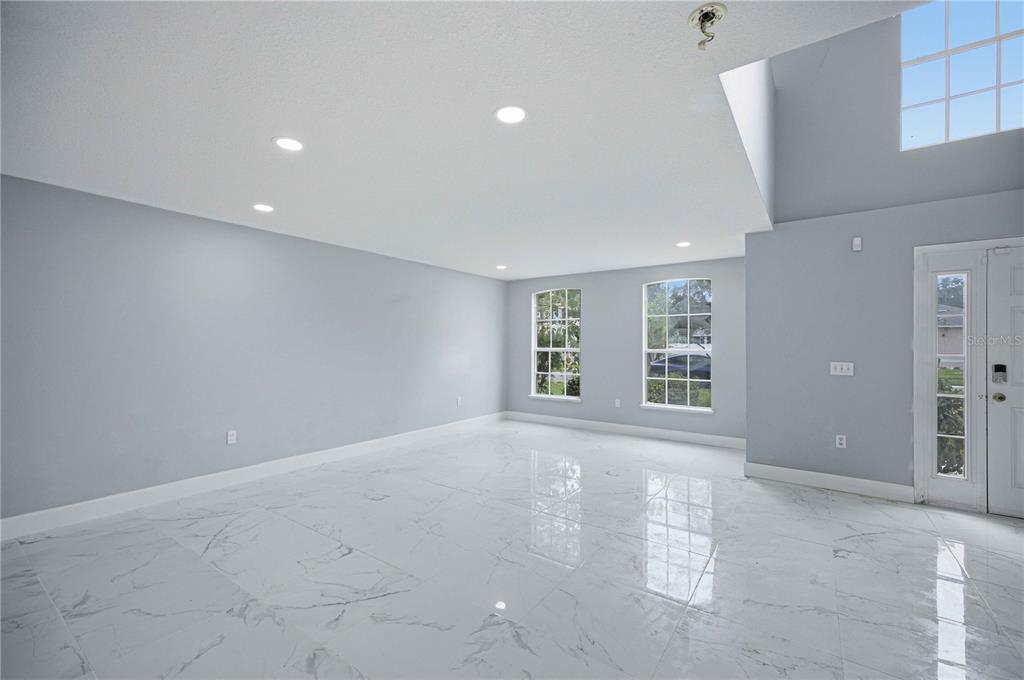A bright, empty room features light gray walls, white marble-look tile flooring, and recessed lighting — 4517 SE 31ST PLACE, OCALA, FL