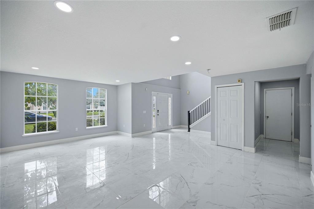 A bright, empty room features white marble-look tile flooring, light gray walls, and a staircase — 4517 SE 31ST PLACE, OCALA, FL
