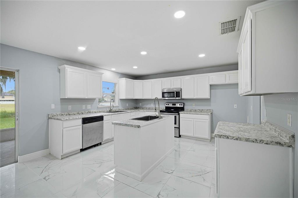 A kitchen with white cabinets, granite countertops, stainless steel appliances, and white marble-patterned tile flooring — 4517 SE 31ST PLACE, OCALA, FL