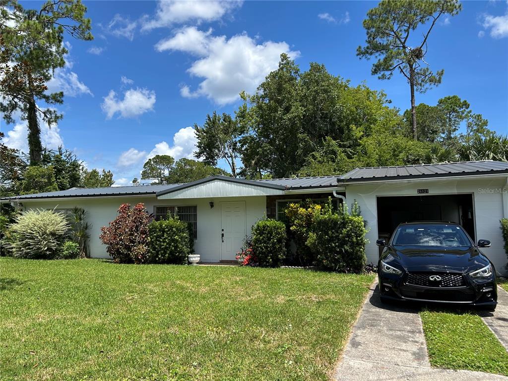 A single-story house with a white exterior, metal roof, and a black car in the carport — 24121 ARMADILLO ROAD, ASTOR, FL