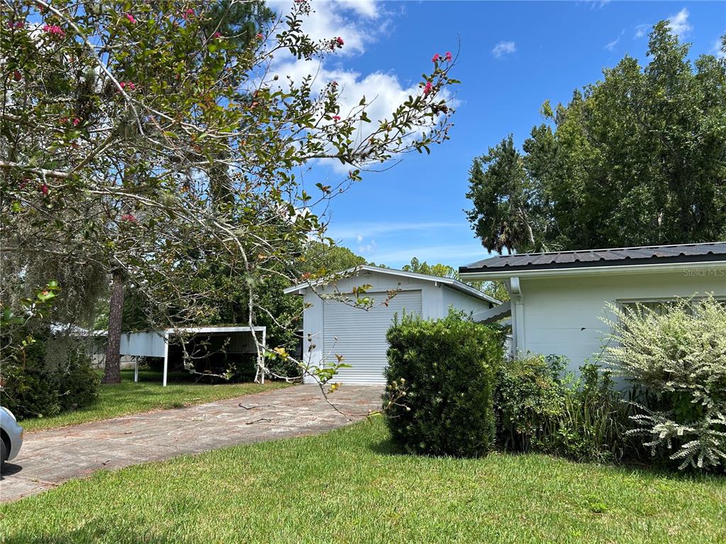 A detached garage and a carport sit on a concrete driveway next to a house — 24121 ARMADILLO ROAD, ASTOR, FL