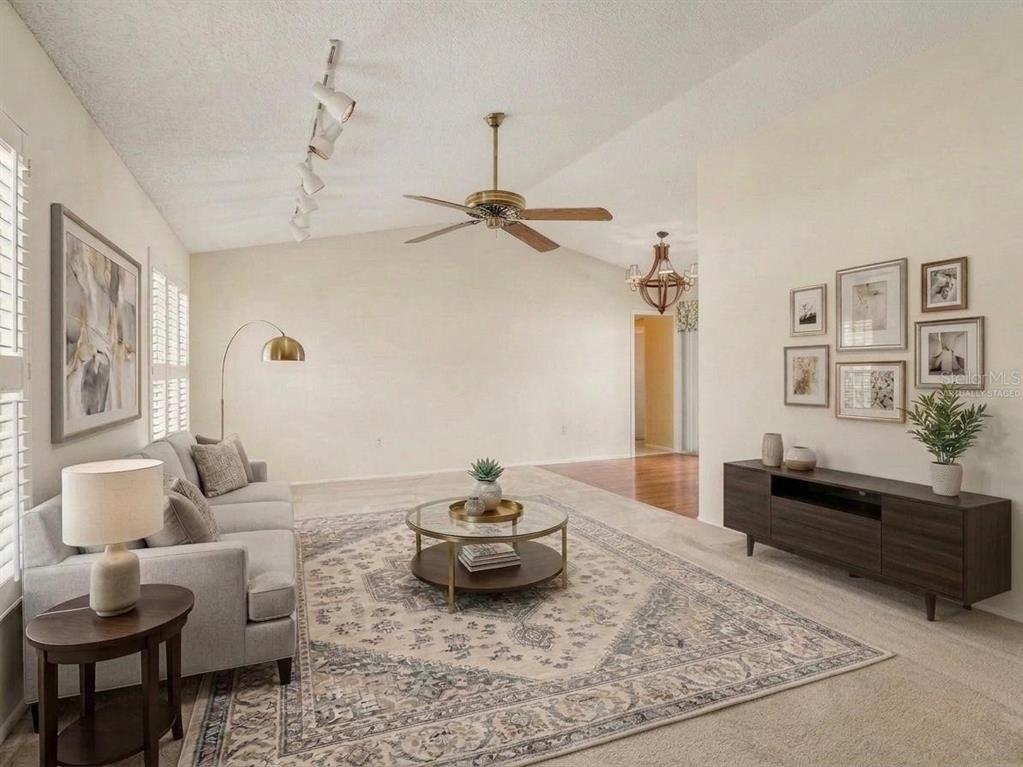 A carpeted living room features a ceiling fan, track lighting, and three windows with shutters — 7207 IMMOKALEE COURT, ORLANDO, FL