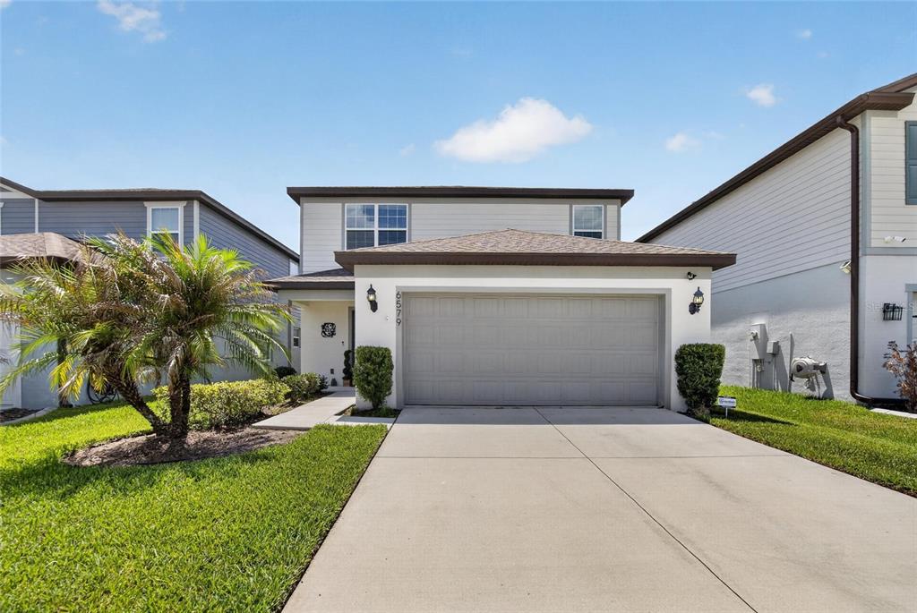 A two-story suburban house features a gray garage door, light siding, and a front lawn — 6579 RYESTONE WAY, WESLEY CHAPEL, FL