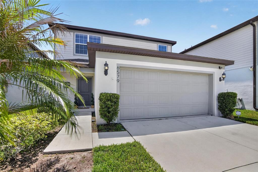 A two-story house features a white stucco facade, a two-car garage, and a palm tree — 6579 RYESTONE WAY, WESLEY CHAPEL, FL