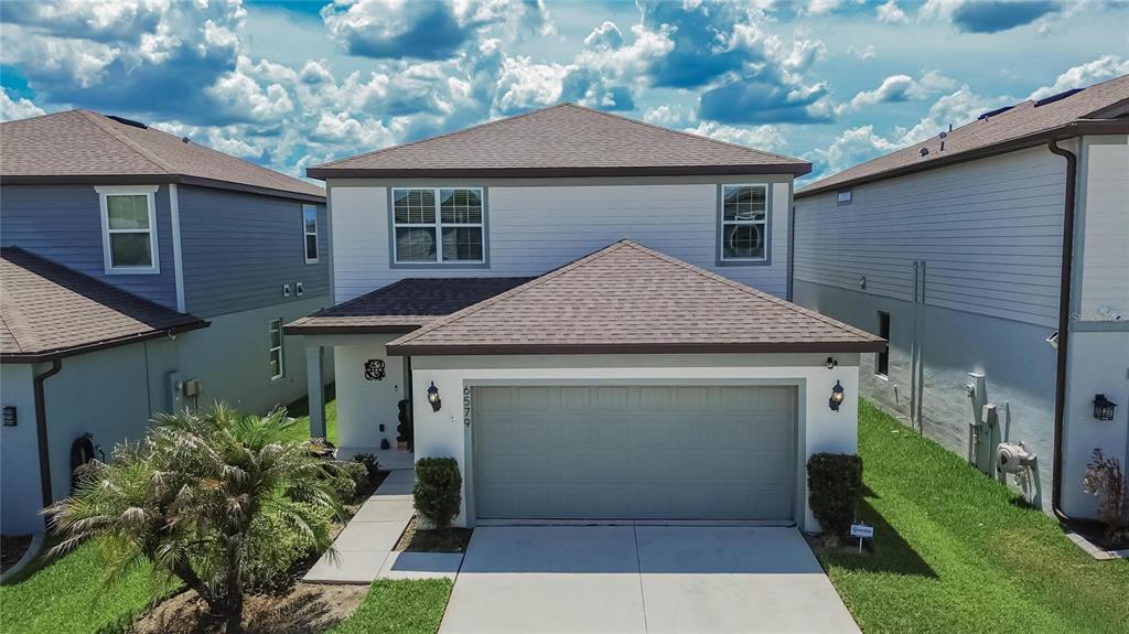 A two-story suburban house with a gray garage, white siding, and a brown shingled roof — 6579 RYESTONE WAY, WESLEY CHAPEL, FL