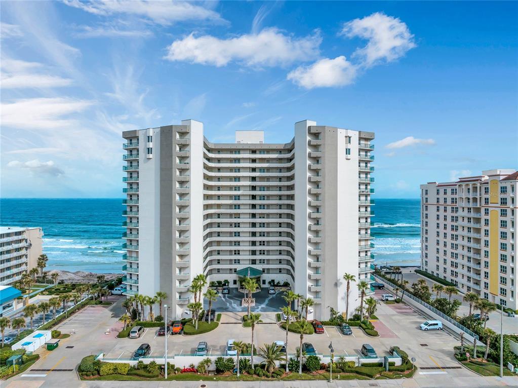 An aerial view shows a tall beachfront condominium building with a parking lot in front — 2055 S ATLANTIC AVENUE UNIT 705, DAYTONA BEACH SHORES, FL