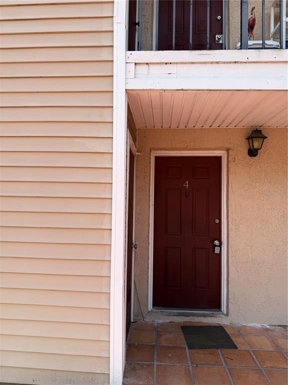 A red front door labeled number four sits under a balcony on a tiled porch — 21026 VOYAGER BOULEVARD UNIT 4, LAND O LAKES, FL