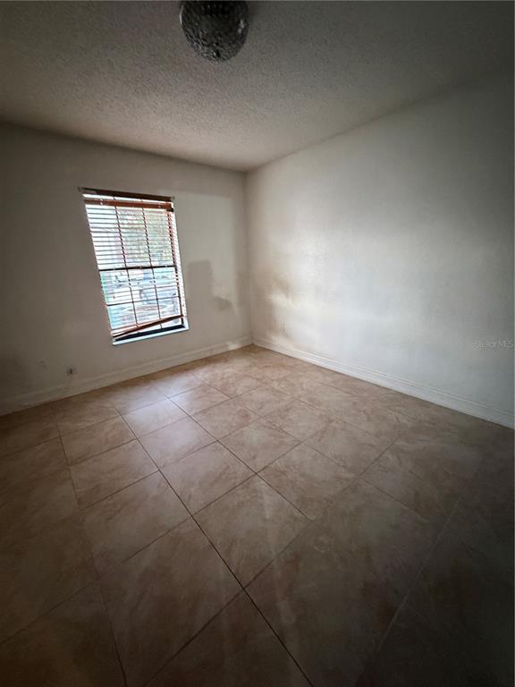 An empty room features light-colored tile flooring, white walls, and a single window with blinds — 21026 VOYAGER BOULEVARD UNIT 4, LAND O LAKES, FL