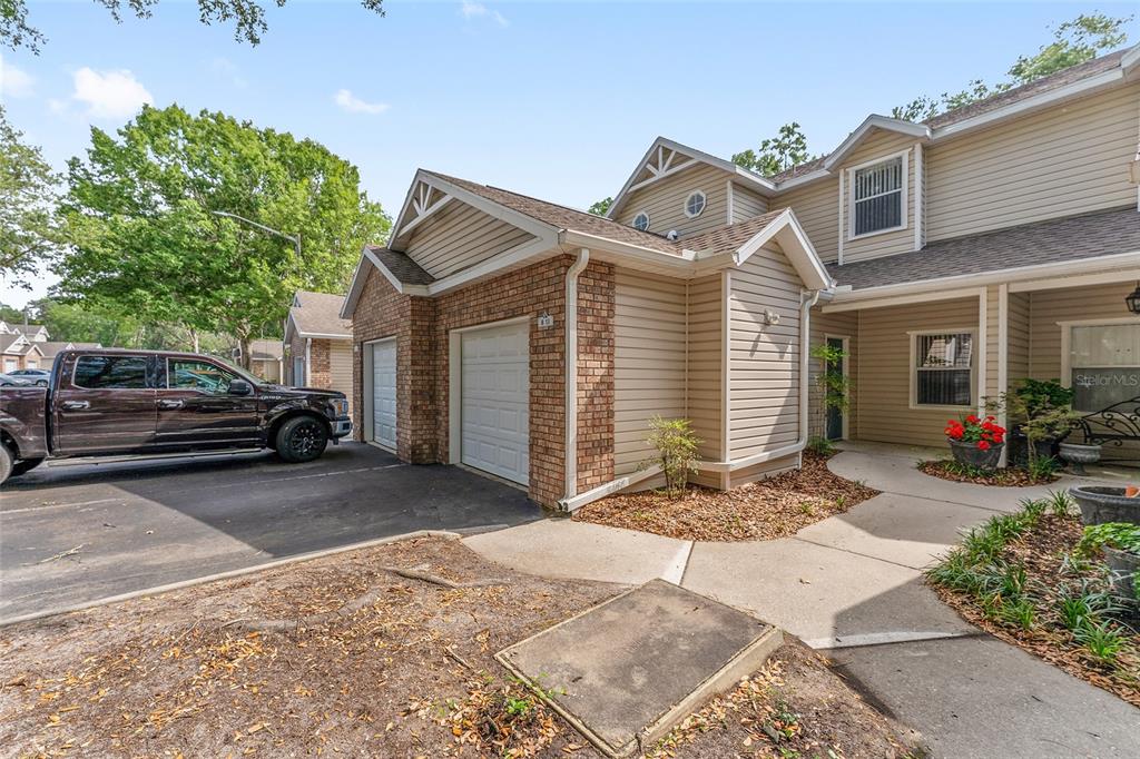 A two-story townhouse exterior features tan siding, brick accents, a two-car garage, and a walkway — 4700 SW ARCHER ROAD UNIT B-13, GAINESVILLE, FL
