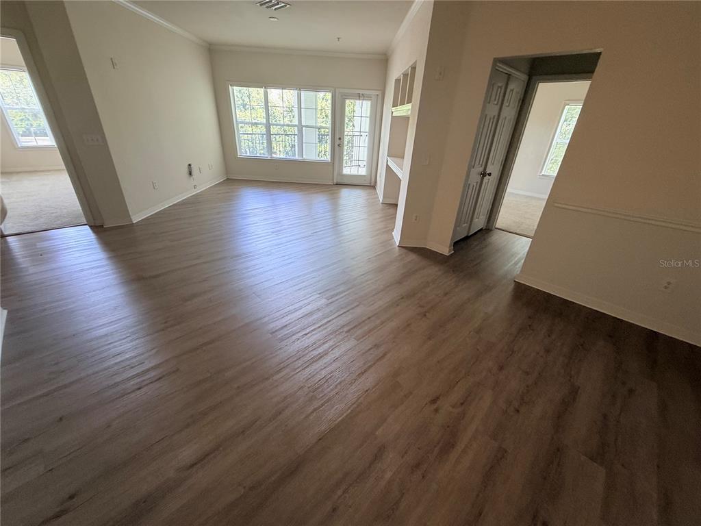 An empty living room features wood-look flooring, white walls, built-in shelving, and a glass door — 3621 CONROY ROAD UNIT 732, ORLANDO, FL
