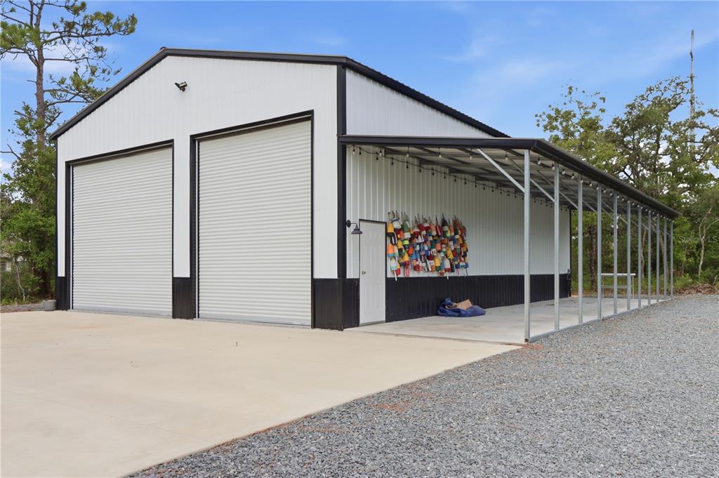 A white metal building with two roll-up garage doors and an attached side carport — 14487 GOLDENEYE ROAD, WEEKI WACHEE, FL