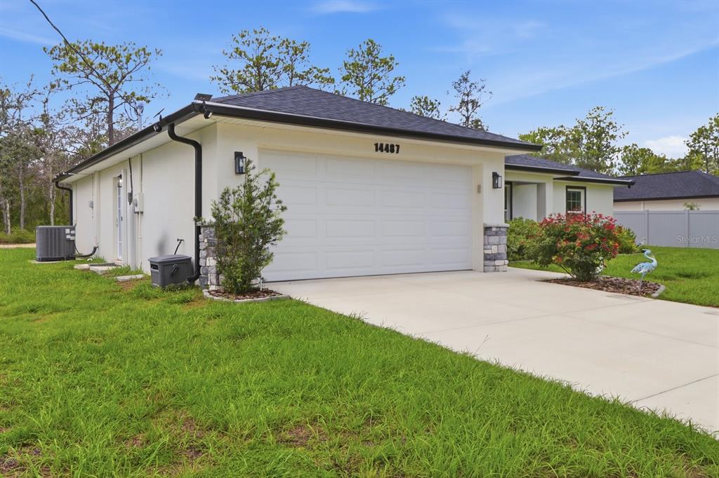 A single-story house exterior features a white stucco facade, a two-car garage, and a lawn — 14487 GOLDENEYE ROAD, WEEKI WACHEE, FL