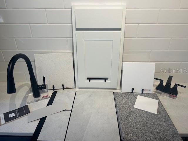A display of interior design samples featuring white cabinets, countertops, tiles, and black plumbing fixtures — 5862 SUNLIT BEND WAY, APOLLO BEACH, FL