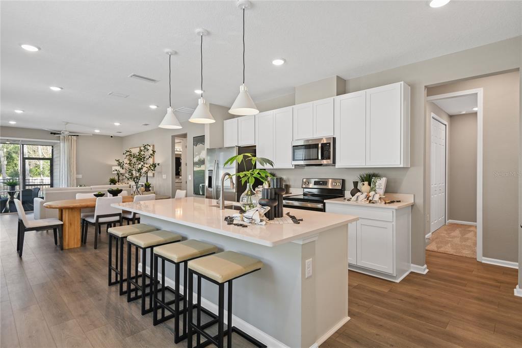 A modern kitchen features a large island with bar seating, white cabinets, and wood flooring — 5862 SUNLIT BEND WAY, APOLLO BEACH, FL