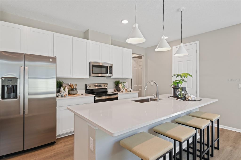 A modern kitchen features white cabinets, stainless steel appliances, a quartz island, and pendant lighting — 5862 SUNLIT BEND WAY, APOLLO BEACH, FL