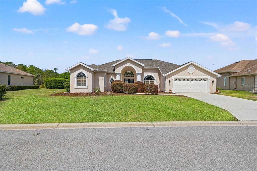 A single-story suburban house with a beige stucco exterior, a two-car garage, and a lawn — 8405 MAYBELLE DRIVE, WEEKI WACHEE, FL