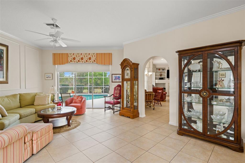 A living room features tile floors, a grandfather clock, a display cabinet, and a pool view — 8405 MAYBELLE DRIVE, WEEKI WACHEE, FL