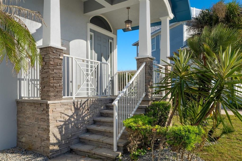 A front porch with stone pillars, white railings, and steps leading to a gray front door — 2 MAR AZUL N, PONCE INLET, FL