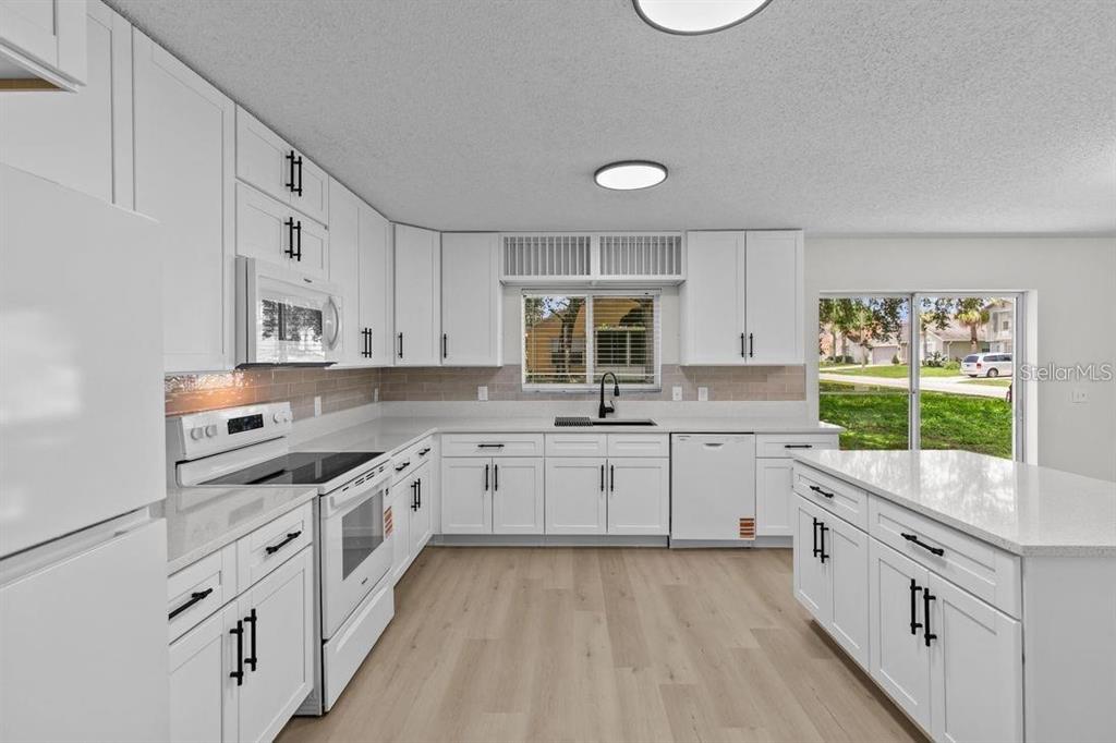 A bright kitchen features white cabinets, quartz countertops, stainless steel appliances, and light wood flooring — 1537 MORNING STAR DRIVE, CLERMONT, FL