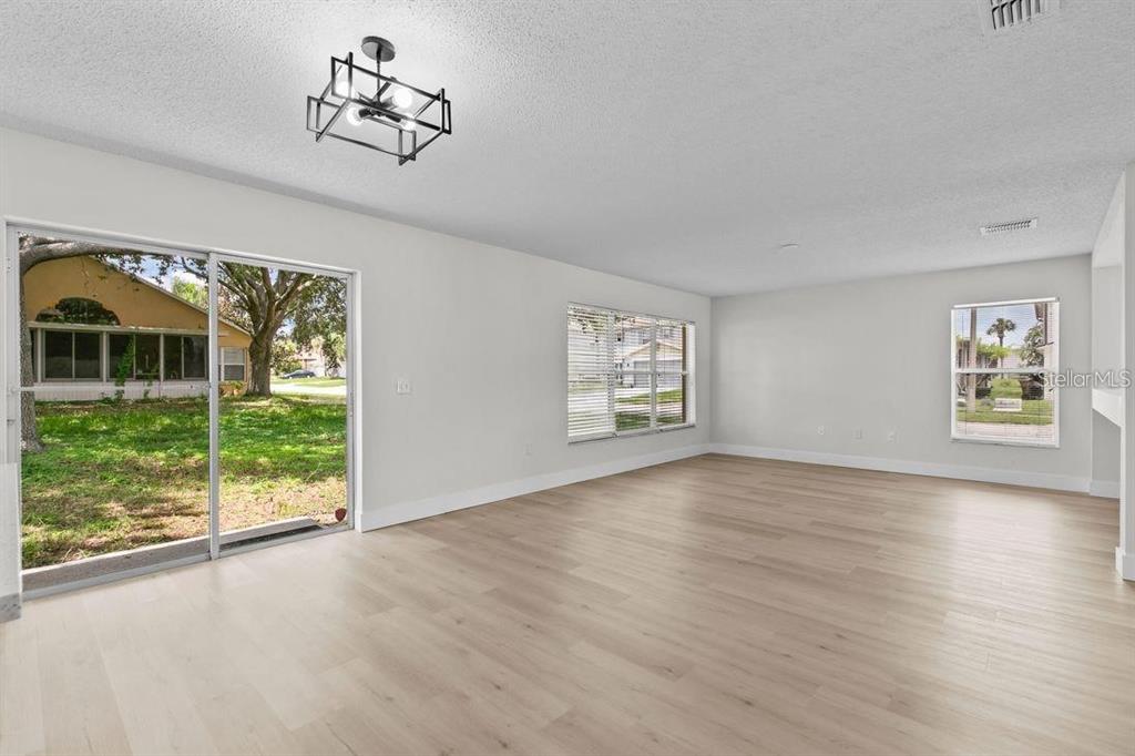 An empty living room with light wood-look flooring, a modern light fixture, and sliding glass doors — 1537 MORNING STAR DRIVE, CLERMONT, FL