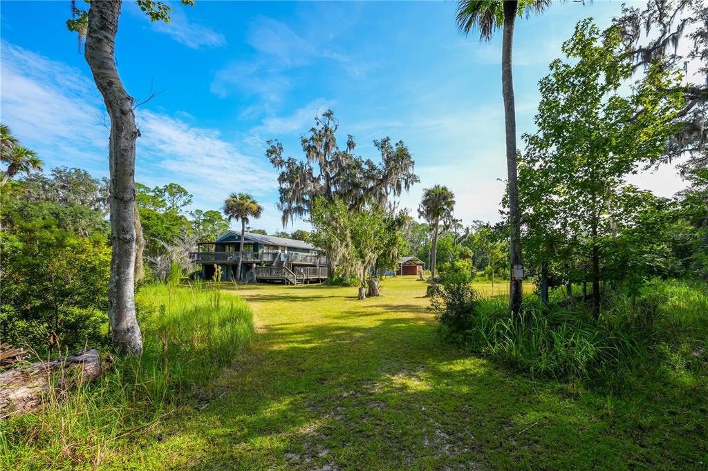 A two-story house with a wooden deck sits on a grassy lot with palm trees — 1879 HIDEAWAY LANE, EDGEWATER, FL