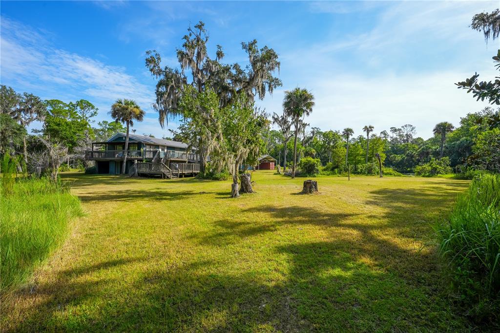 A two-story house with a large wooden deck sits on a grassy lot with trees — 1879 HIDEAWAY LANE, EDGEWATER, FL