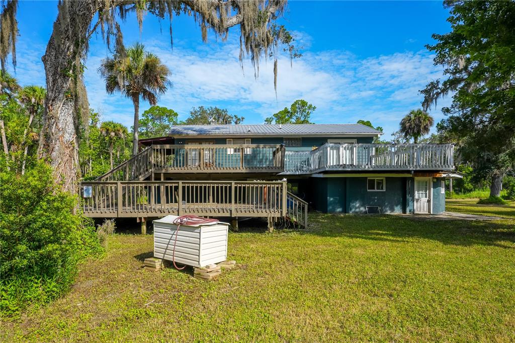 A two-story house with a large wooden deck and a metal roof in a yard — 1879 HIDEAWAY LANE, EDGEWATER, FL