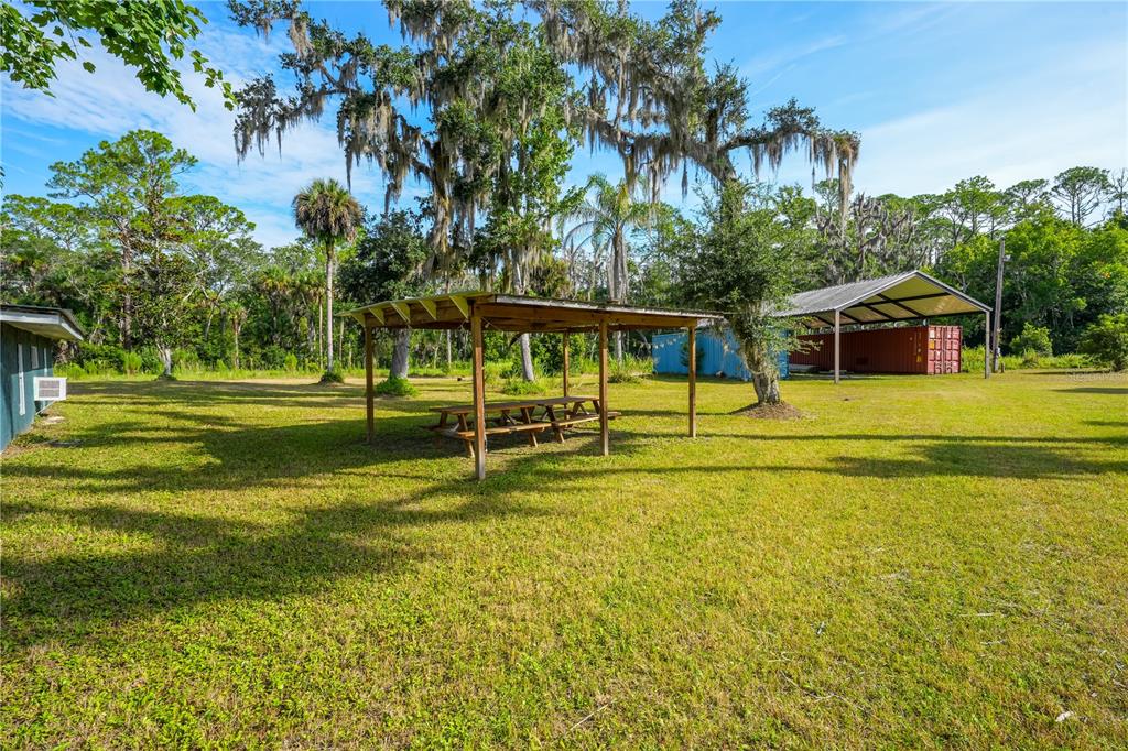 A grassy backyard features a wooden picnic pavilion, a metal storage structure, and mature trees — 1879 HIDEAWAY LANE, EDGEWATER, FL