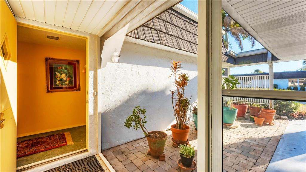 A yellow door opens into an entryway next to a brick-paved patio with potted plants — 3823 GLEN OAKS DRIVE E UNIT 83, SARASOTA, FL