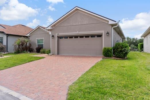 A single-story house with a beige stucco exterior, a two-car garage, and a brick driveway — 1108 SAWGRASS DRIVE, WINTER HAVEN, FL