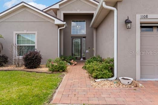 A beige house exterior features a brick walkway leading to the front door and garage — 1108 SAWGRASS DRIVE, WINTER HAVEN, FL
