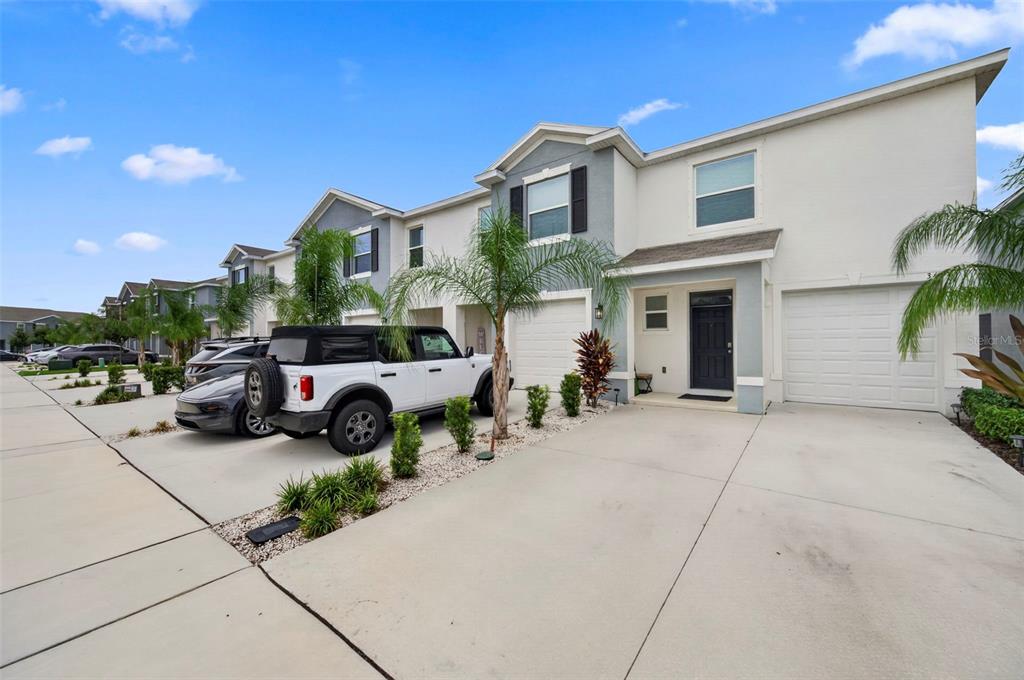 A row of two-story townhouses with white stucco exteriors, attached garages, and paved driveways — 369 MANGROVE SHADE CIRCLE, APOLLO BEACH, FL