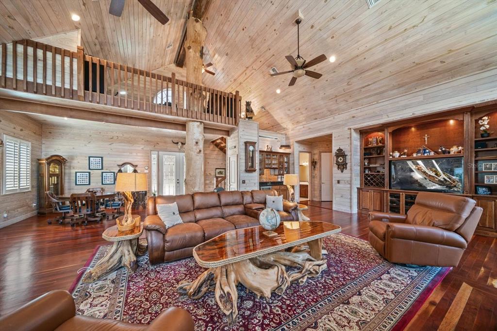 A rustic living room features wood-paneled walls, a loft, and a central tree trunk pillar — 7650 N WHIPPOORWILL TERRACE, HERNANDO, FL