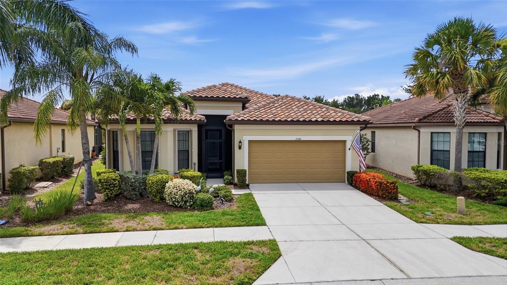A single-story house with a tan stucco exterior, tile roof, and a two-car garage — 2543 ARUGULA DRIVE, NORTH PORT, FL