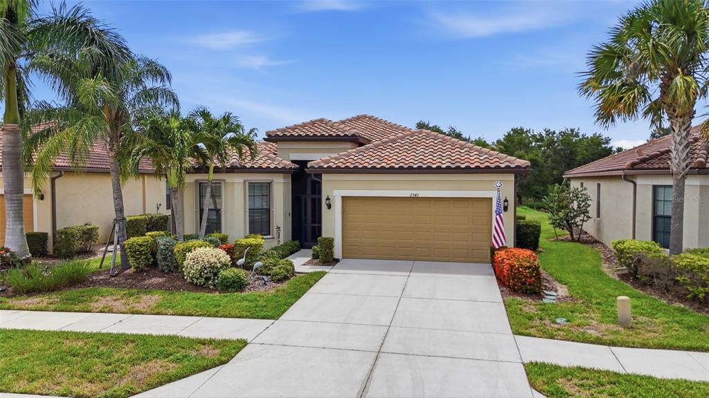 A single-story house with a tan stucco exterior, tile roof, and a two-car garage — 2543 ARUGULA DRIVE, NORTH PORT, FL