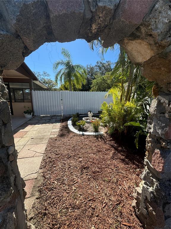 A stone archway frames a view of a backyard with a patio, mulch, and fountain — 5608 GATEWAY DRIVE, TAMPA, FL