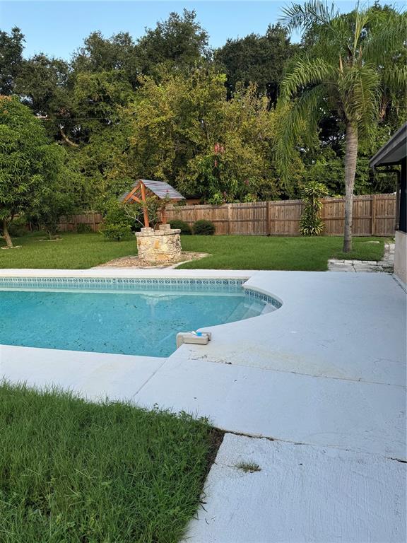 A backyard features a swimming pool, a stone wishing well, and a wooden privacy fence — 5608 GATEWAY DRIVE, TAMPA, FL