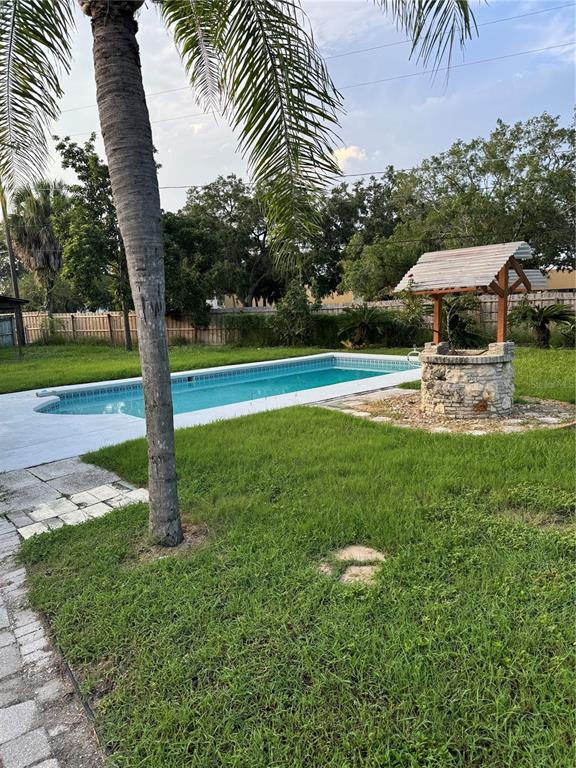 A backyard features a rectangular swimming pool, a stone wishing well, and a palm tree — 5608 GATEWAY DRIVE, TAMPA, FL