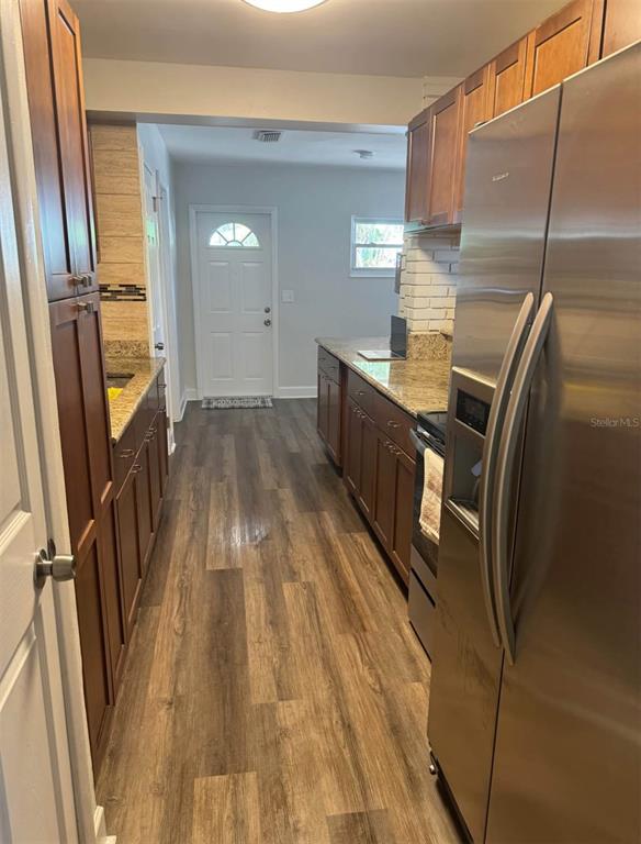 A galley kitchen features wood cabinets, granite countertops, stainless steel appliances, and wood-look flooring — 5608 GATEWAY DRIVE, TAMPA, FL