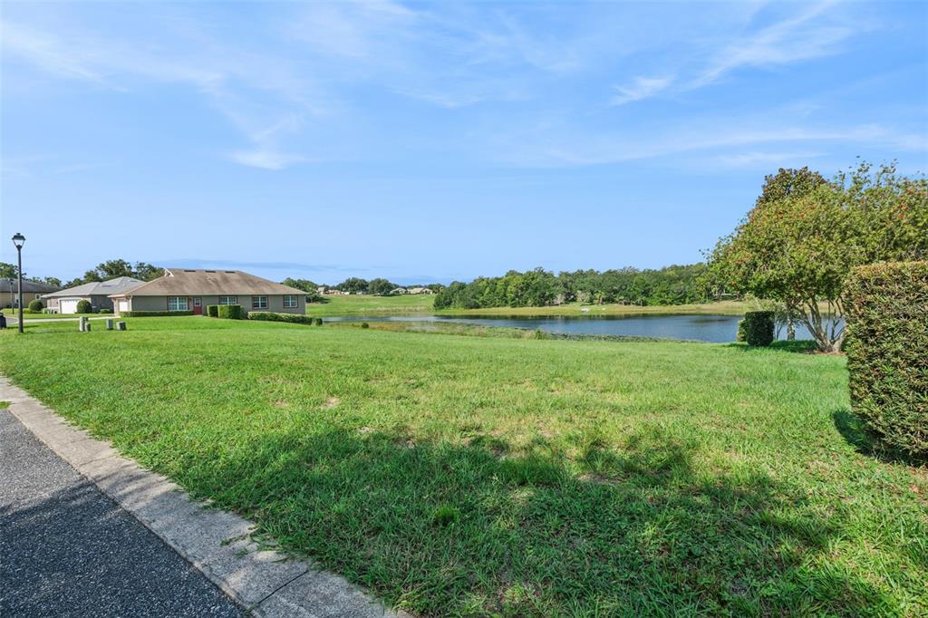 A grassy yard overlooks a pond with trees and houses in the background — 77 FAIRWAY CIRCLE UNIT 101, UMATILLA, FL