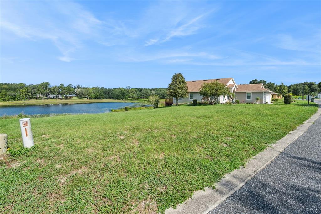 A grassy lot slopes down toward a pond next to a single-story suburban house — 77 FAIRWAY CIRCLE UNIT 101, UMATILLA, FL