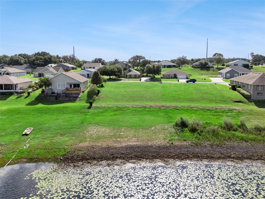 An aerial view shows a grassy lot situated between suburban houses and a lily-covered pond — 77 FAIRWAY CIRCLE UNIT 101, UMATILLA, FL