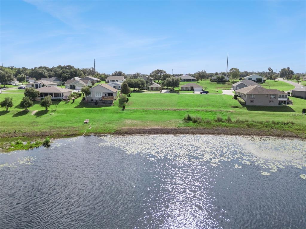 An aerial view shows a grassy lot situated between several houses and a pond — 77 FAIRWAY CIRCLE UNIT 101, UMATILLA, FL
