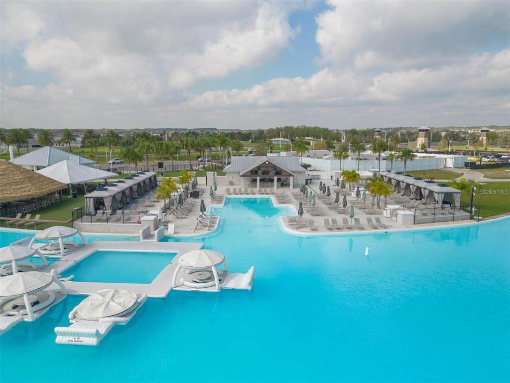 An aerial view shows a large turquoise swimming pool with cabanas and a clubhouse — 8377 CLAW GLADES LOOP, WESLEY CHAPEL, FL