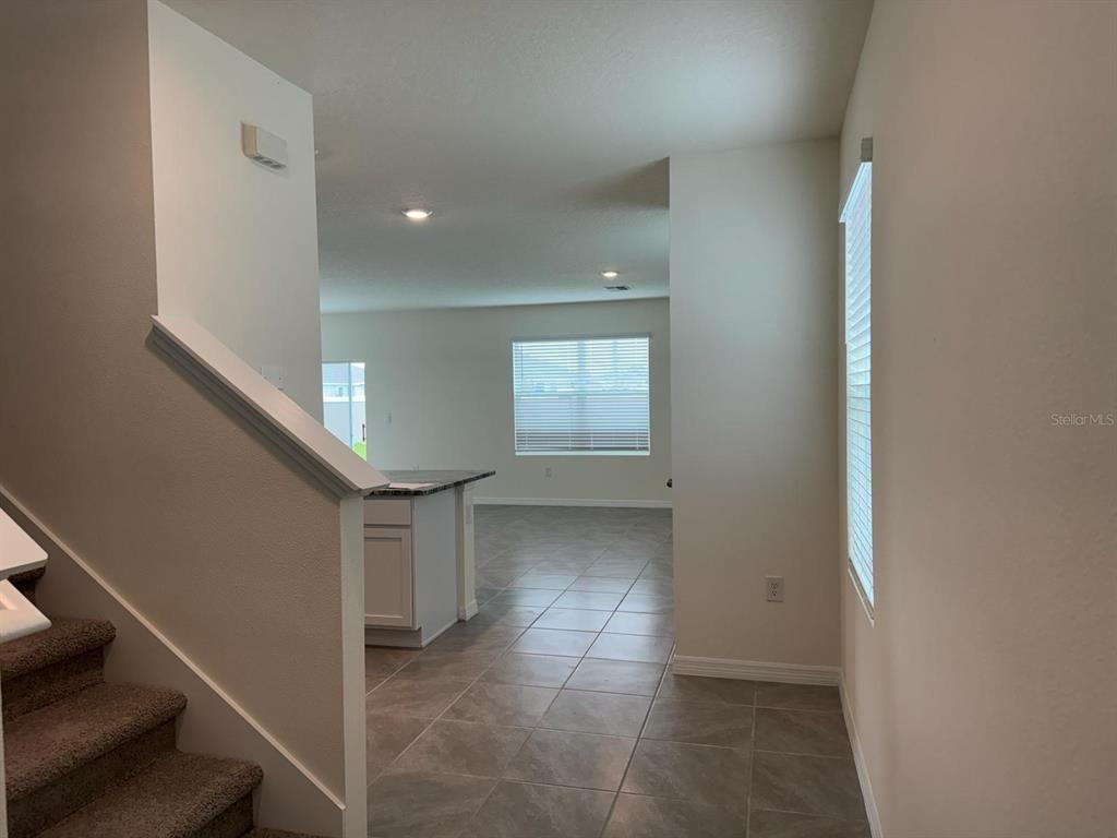 A view from the bottom of a carpeted staircase looking toward a tiled kitchen area — 8377 CLAW GLADES LOOP, WESLEY CHAPEL, FL