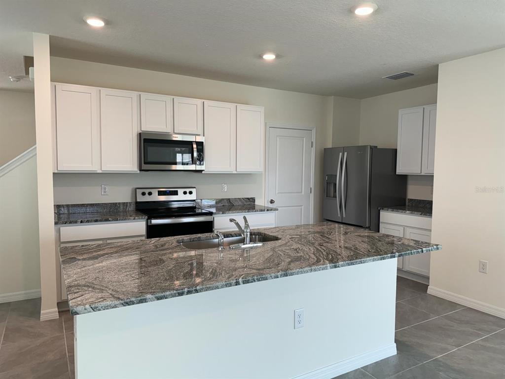 A kitchen features white cabinets, granite countertops, a large island, and stainless steel appliances — 8377 CLAW GLADES LOOP, WESLEY CHAPEL, FL