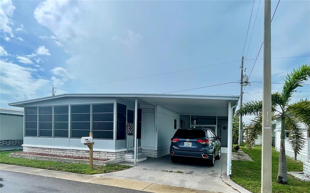 A single-story manufactured home with a screened-in porch, carport, and a dark SUV parked underneath — 34645 CAMPHOR DRIVE N, PINELLAS PARK, FL