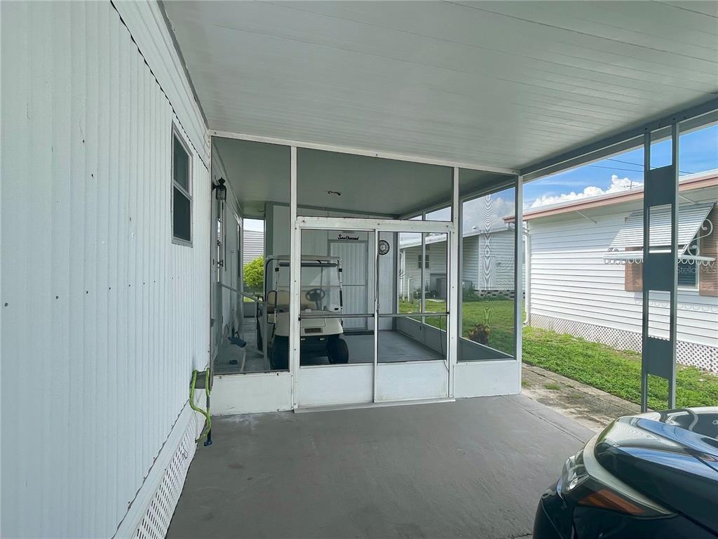 A covered concrete carport features a screened-in porch area with a golf cart inside — 34645 CAMPHOR DRIVE N, PINELLAS PARK, FL