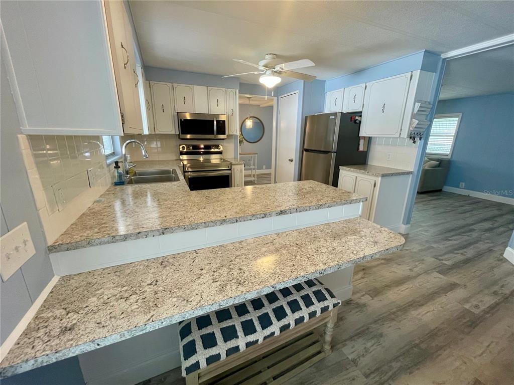 A kitchen features white cabinets, granite countertops, stainless steel appliances, and a breakfast bar — 34645 CAMPHOR DRIVE N, PINELLAS PARK, FL